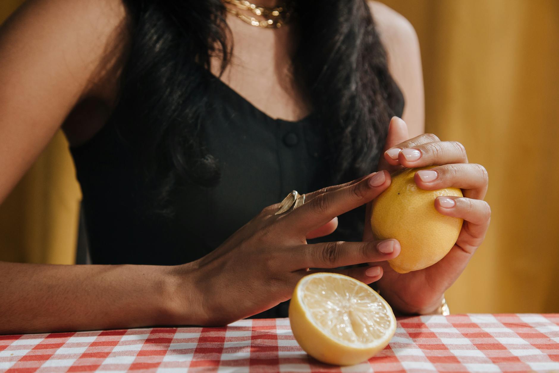 Close-up of a woman holding a fresh lemon at a dining table, symbolizing the tactile focus of clitoral sensation recovery.