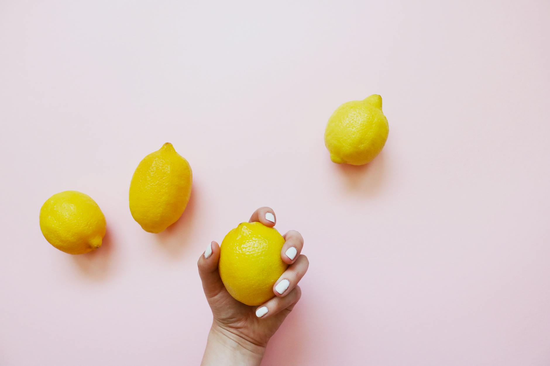 A hand holding a lemon on a soft pink background, symbolizing freshness and the ease of introducing new elements to intimate relationships