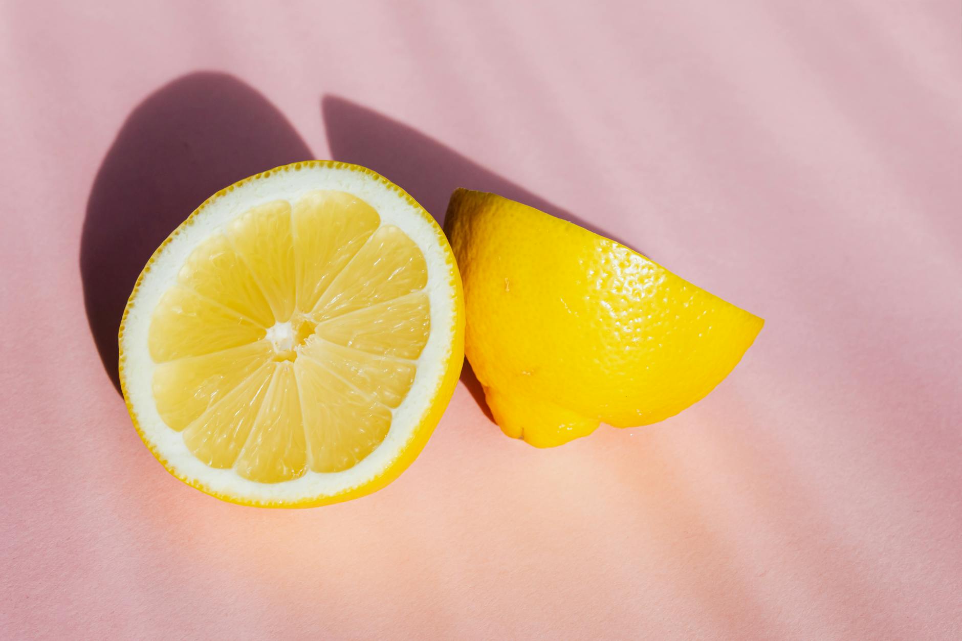 Fresh lemon halves on a bright pink background with natural sunlight