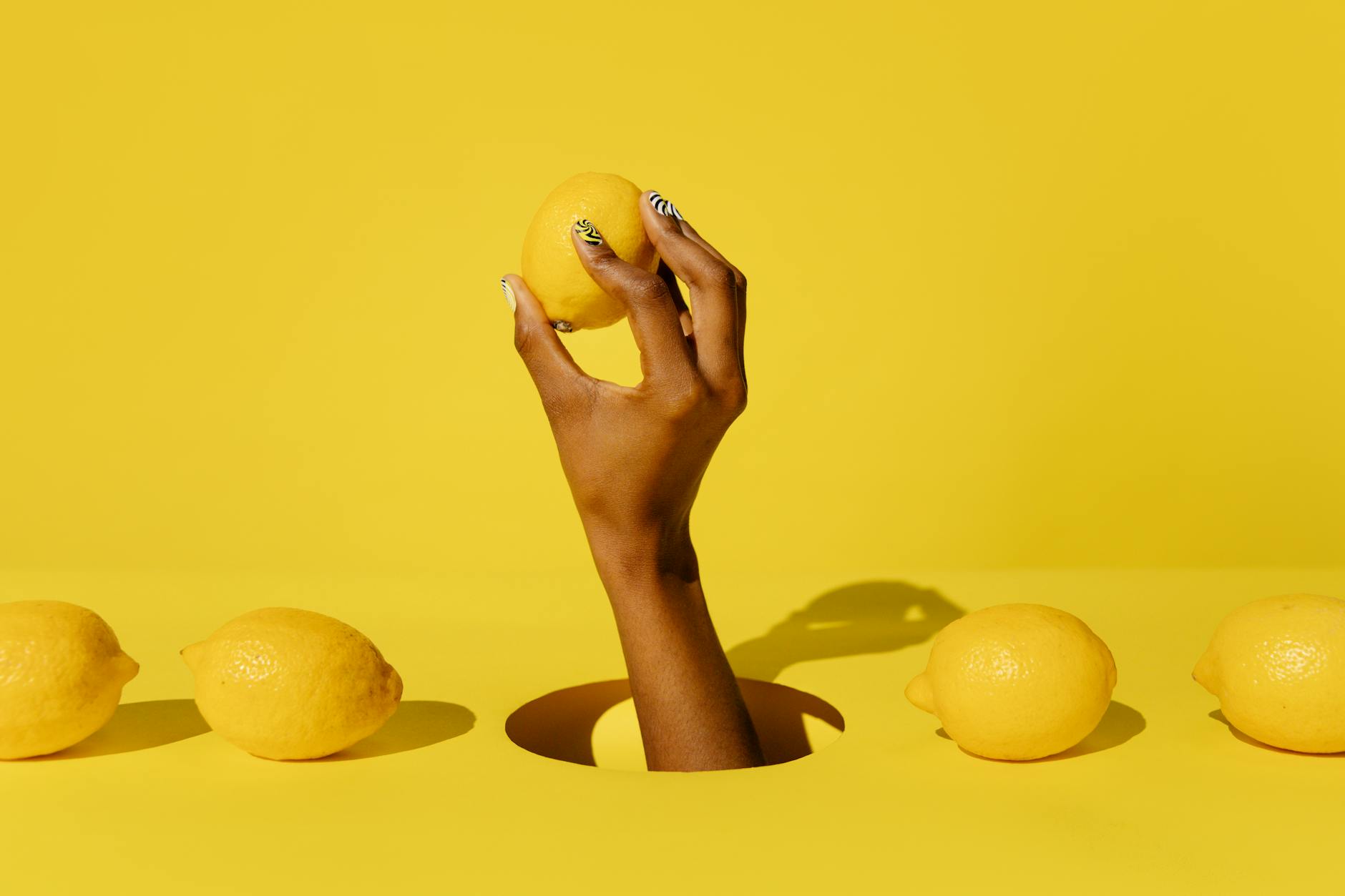 A hand holding a fresh lemon against a bright yellow background, symbolizing the concentrated, targeted stimulation of lemon clitoral vibrators