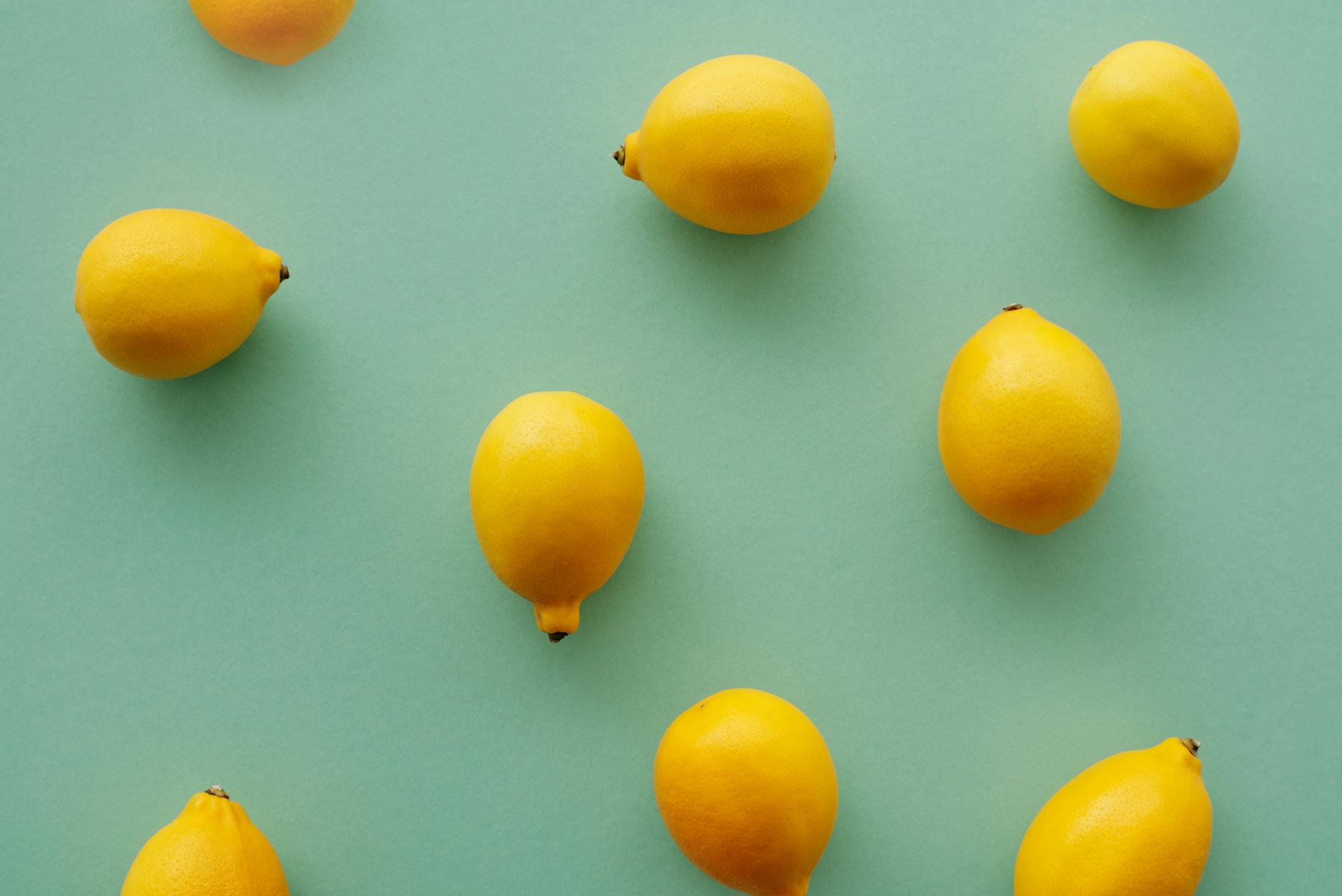 Hand holding a fresh lemon on a soft pink background