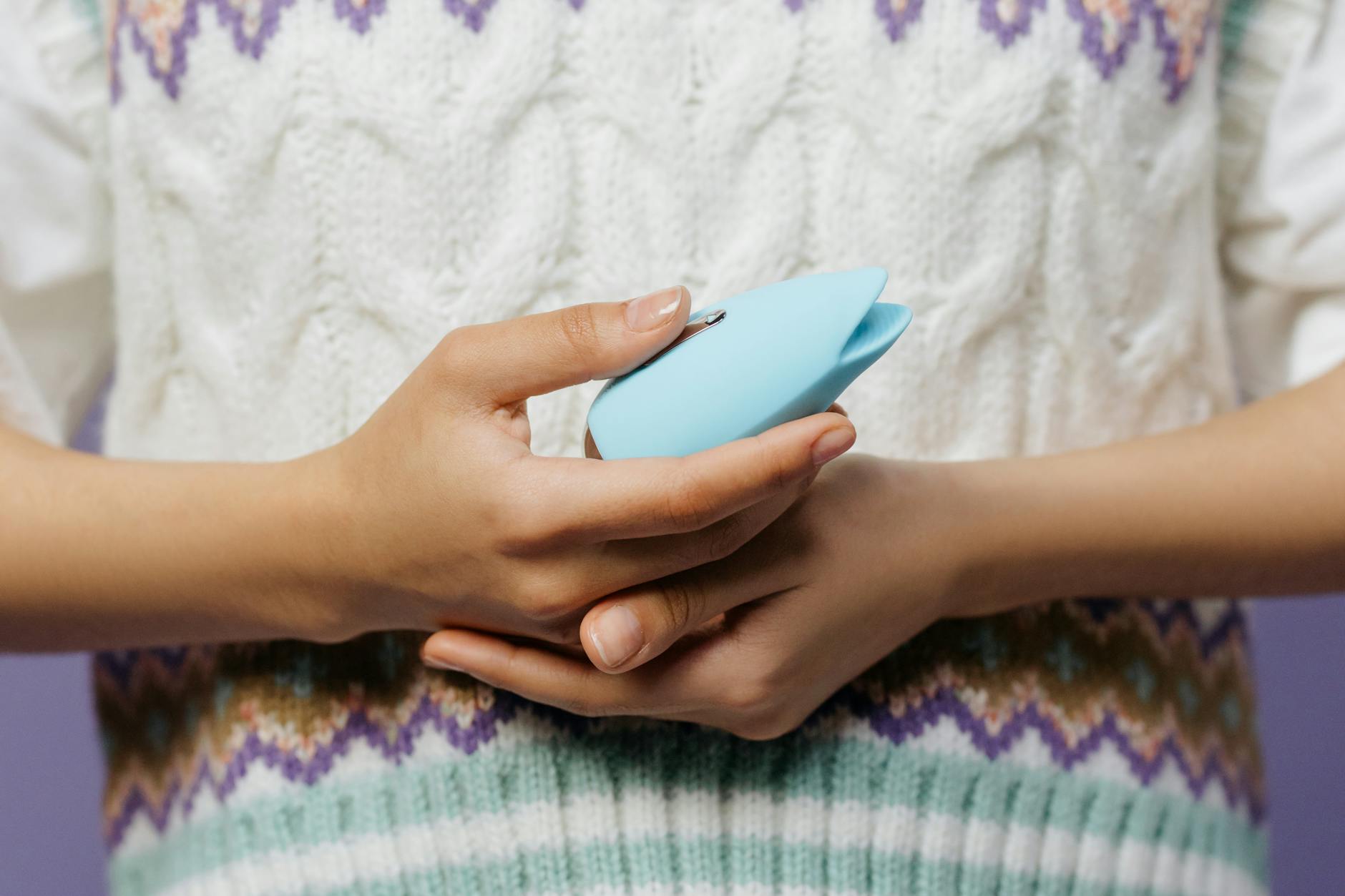 Close-up of hands holding a blue personal massager against a knitted sweater, representing rebuilding sensation and pleasure.