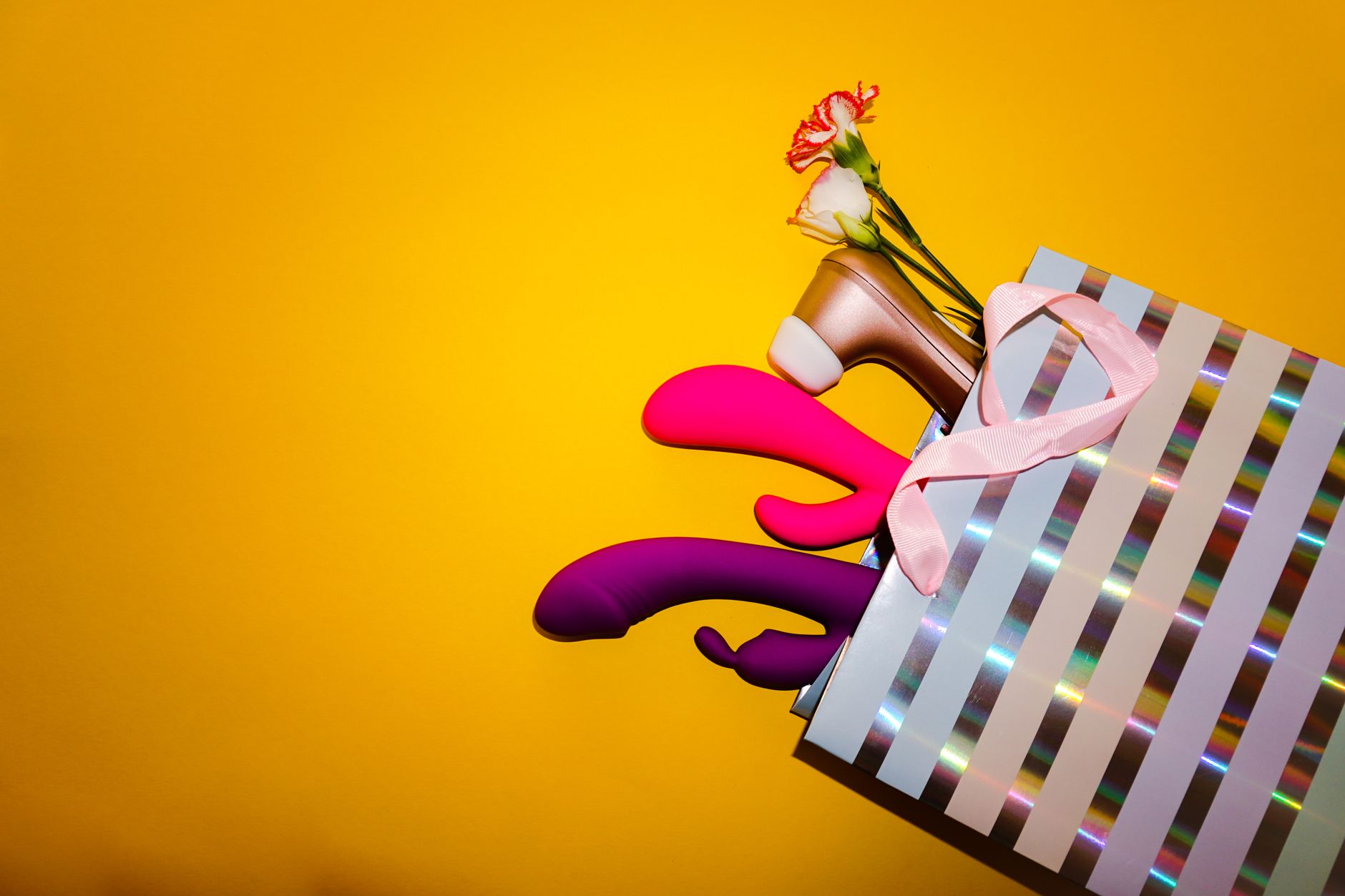 Colorful vibrators with flowers in a holistic gift bag on a bold yellow background
